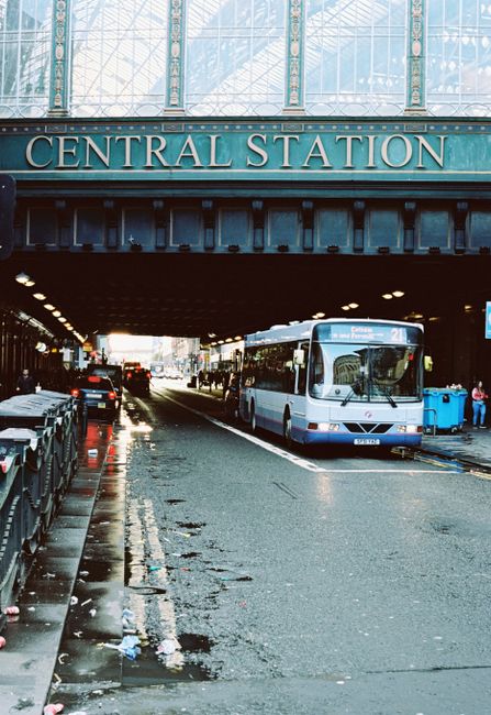 Street view of a bus passing under Glasgow's Central Station on a city road.