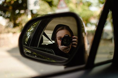 Free Close-up of a woman taking a selfie using DSLR camera in car side mirror reflection. Stock Photo
