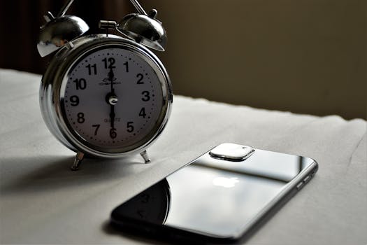 A classic silver alarm clock and modern smartphone placed side by side on a light surface.