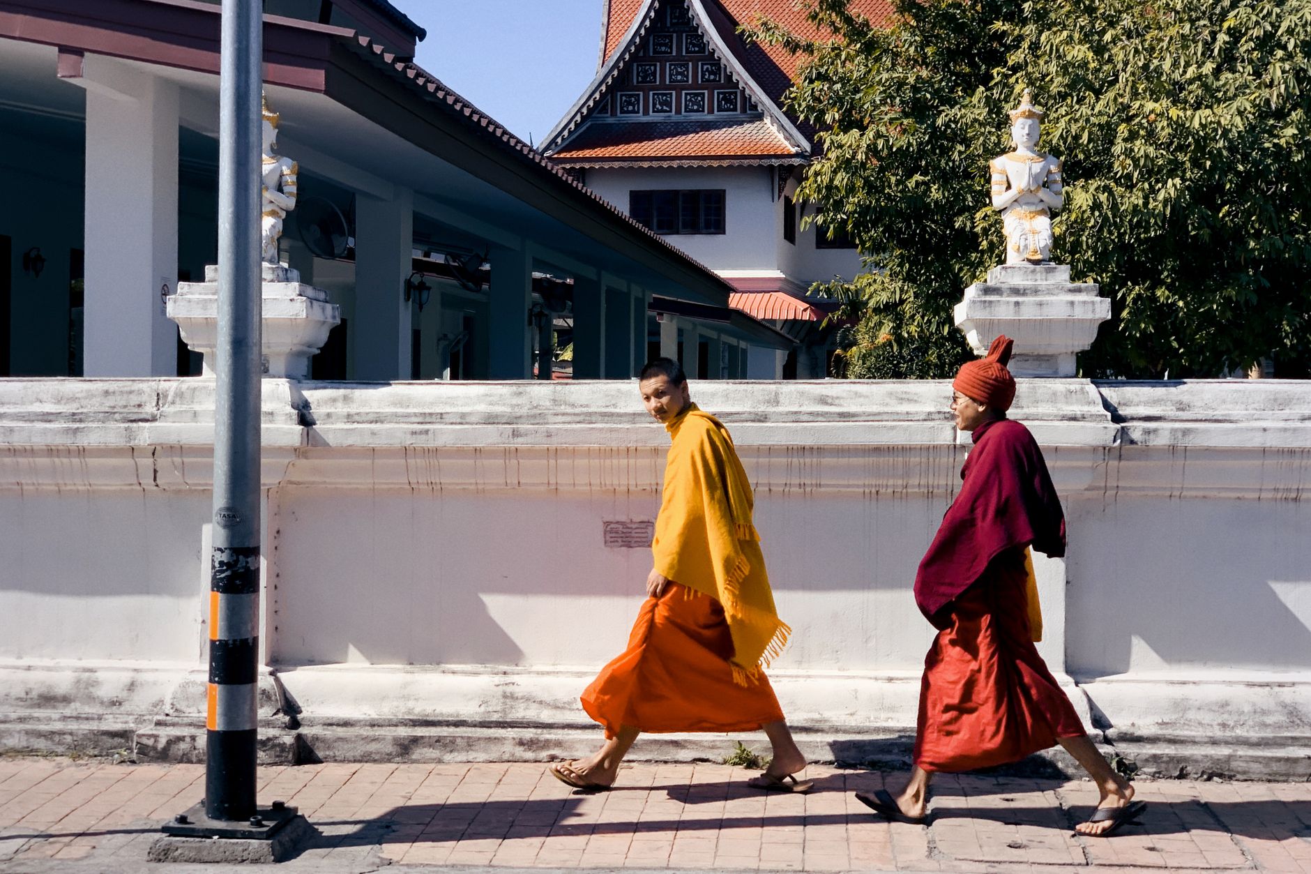 Two monks walking along a temple in Chiang Mai, Thailand, wearing saffron robes.