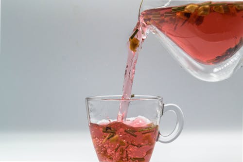 Herbal tea with dried leaves and fruit pouring from glass teapot into cup