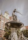 Low angle of famous historic Neptune s Fountain with sculptures and ornamental elements located on square near aged buildings against cloudy sky in Gdansk