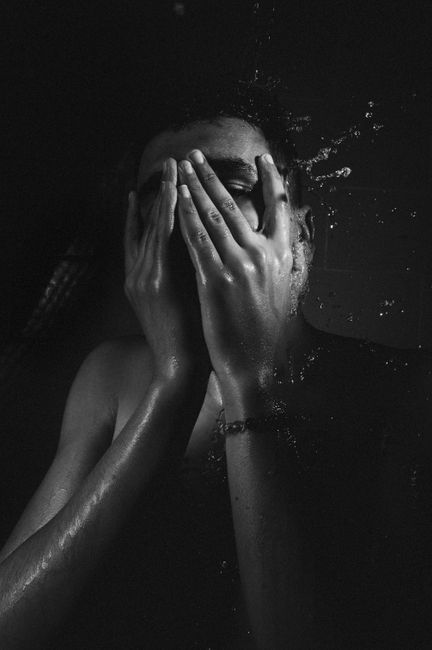 Artistic black and white portrait of a person covering their face with water splashing around.