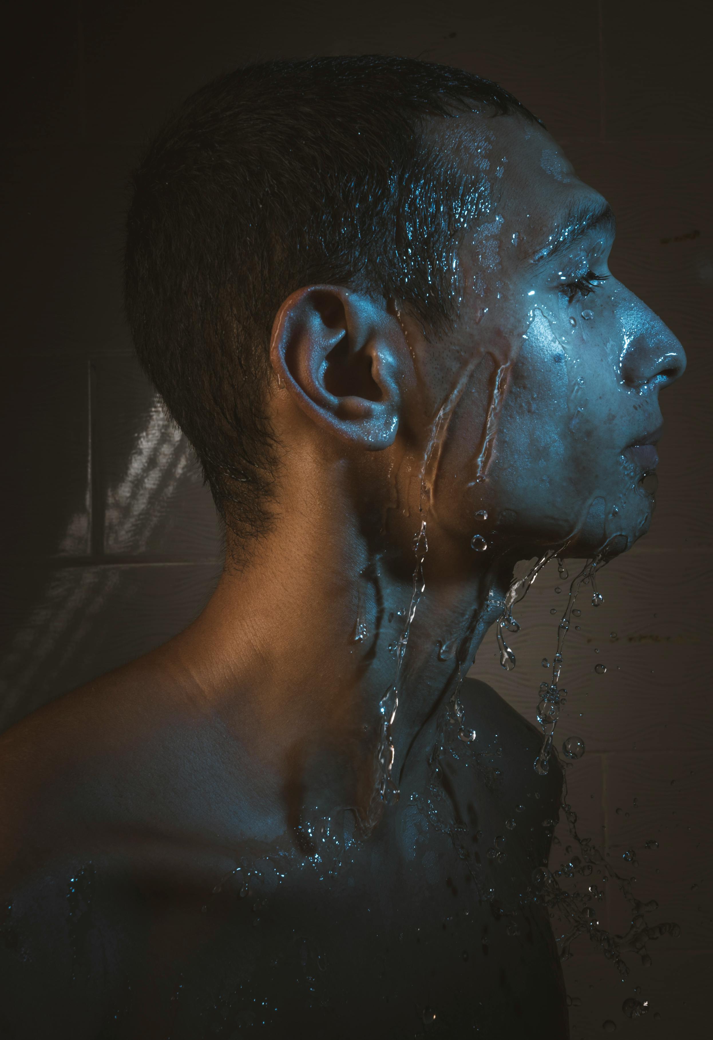 Side profile of a man with water splashing on his face, creating a dramatic and moody effect.