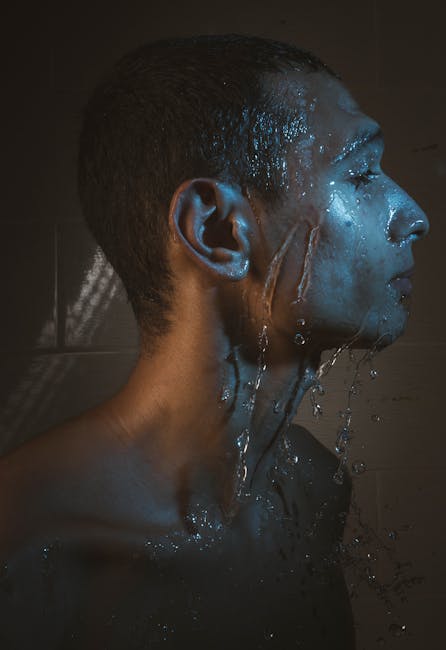 Side profile of a man with water splashing on his face, creating a dramatic and moody effect.