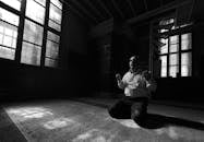 Anonymous ethnic man praying on knees in temple