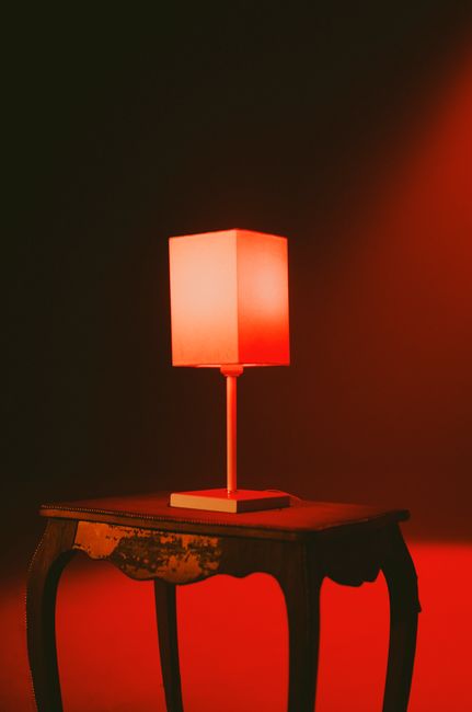 A retro lamp on a rustic wooden table casting a warm red glow in an indoor setting.