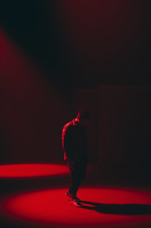 Full body silhouette of anonymous tired male walking in dark room with red illumination