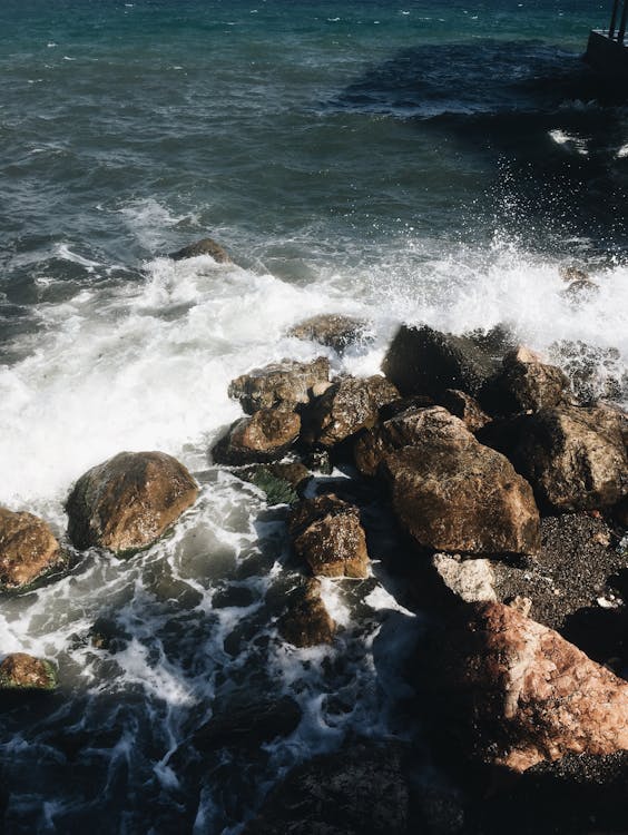 From above of foamy waves of powerful ocean splashing near rough rocky coast on sunny day