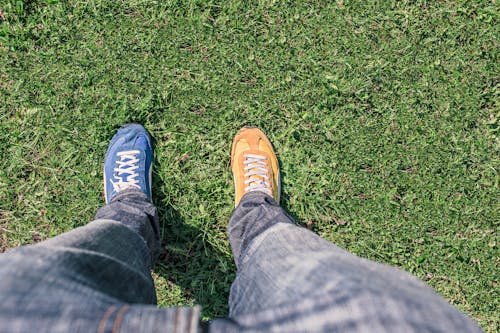 Person Wearing Unpaired Running Shoes Standing on Green Grass