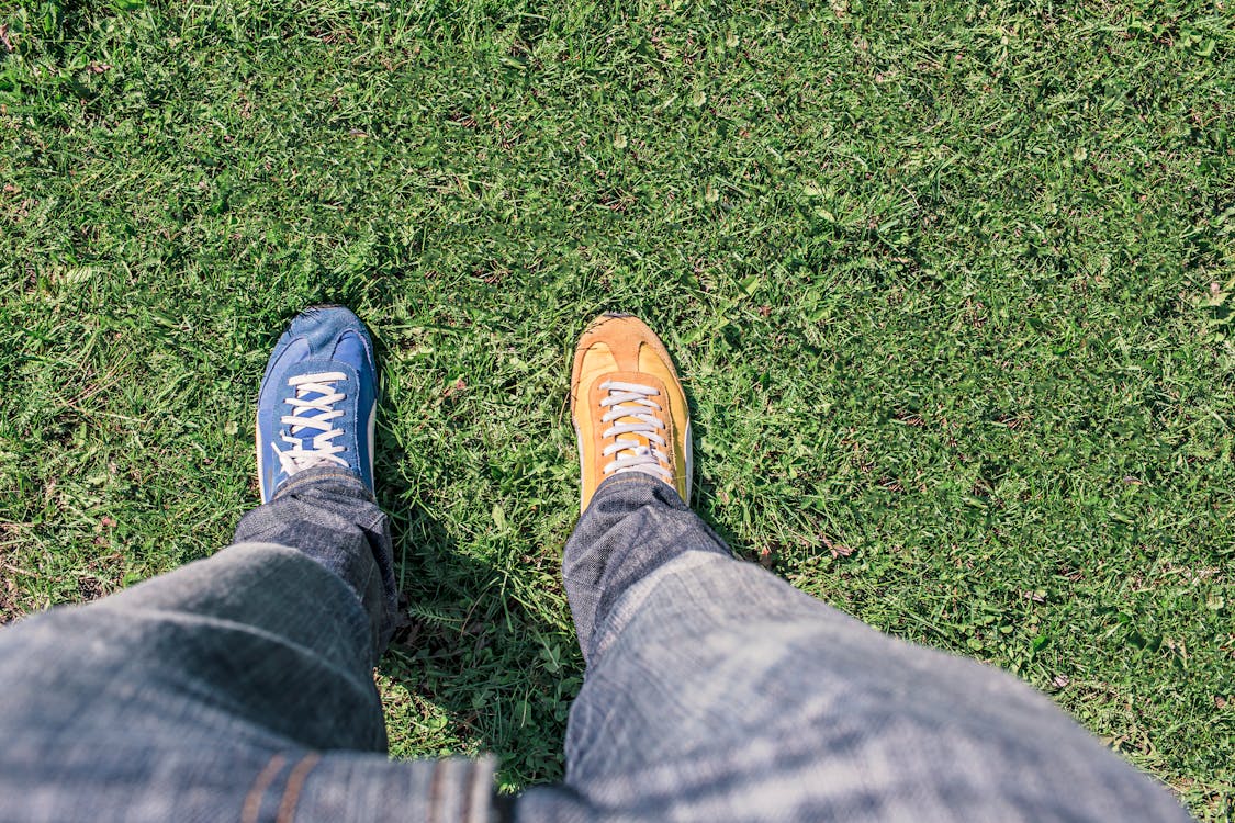 Person Wearing Unpaired Running Shoes Standing on Green Grass