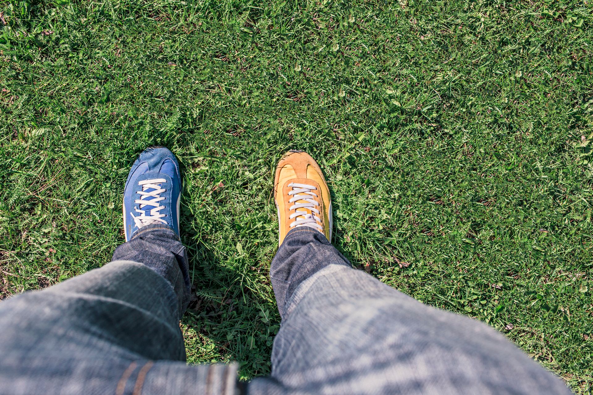 A person wearing mismatched shoes stands on green grass, highlighting differences and individuality.