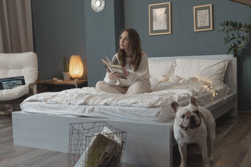 Free Woman Sitting on Bed while Holding a Book Stock Photo