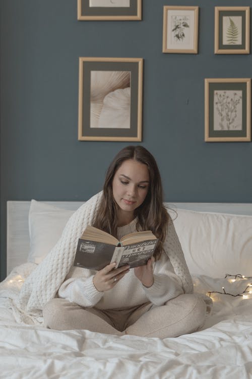 Free Woman Sitting on Bed while Reading a Book Stock Photo