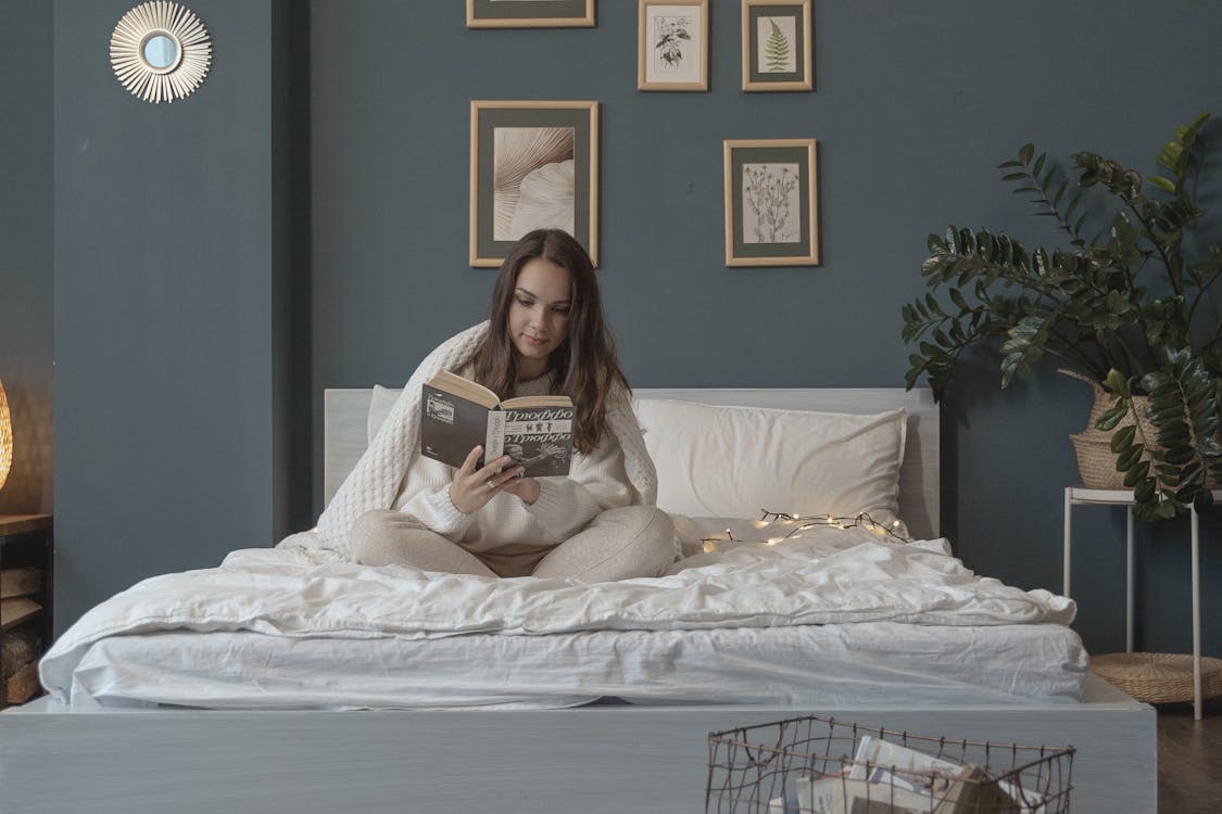 Free Woman Sitting on Bed while Reading a Book Stock Photo
