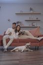 一对夫妇和一只法国斗牛犬在沙发上悠闲地待着，在室内看看书、玩玩手机