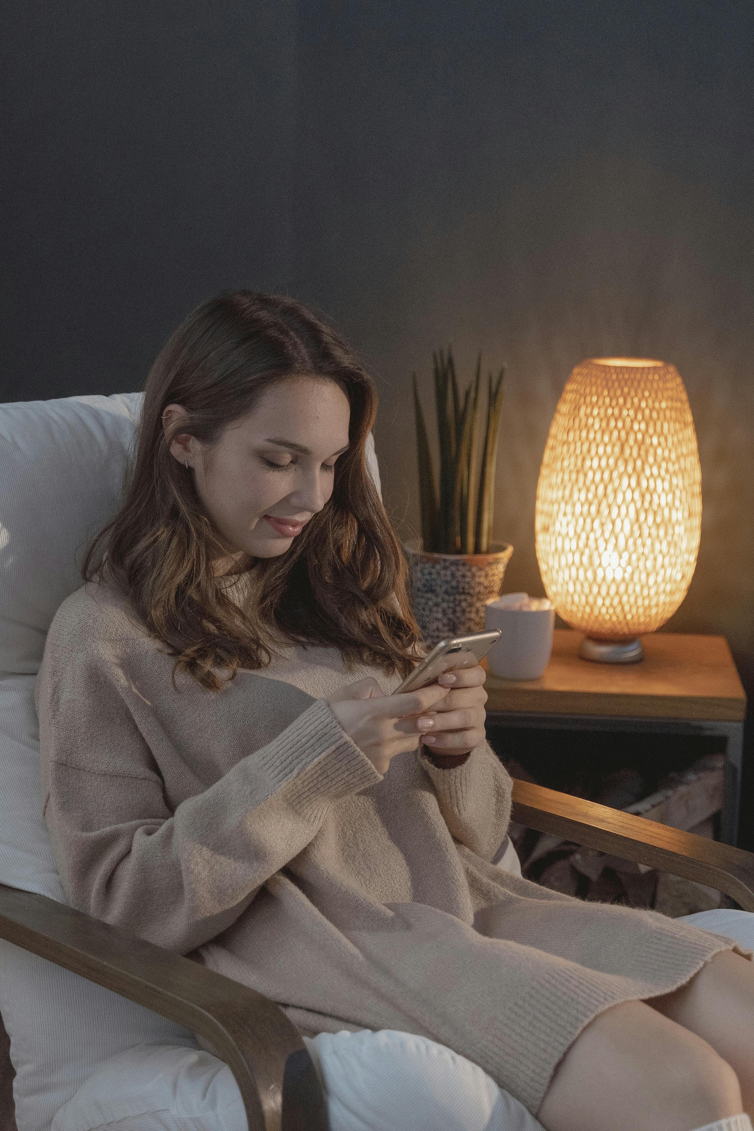 女人坐在舒适的客厅里，一边放松地靠在扶手椅上，一边浏览着智能手机