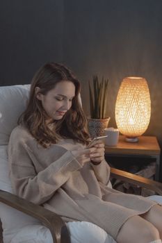 女人坐在舒适的客厅里，一边放松地靠在扶手椅上，一边浏览着智能手机