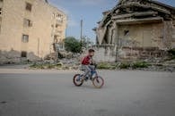 Full body side view of boy in casual clothing riding on bicycle along old ruined construction in daytime