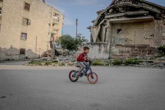 Full body side view of boy in casual clothing riding on bicycle along old ruined construction in daytime