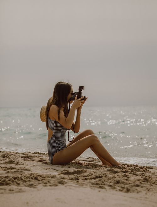 Free Side view of unrecognizable young slim female tourist with long hair in swimwear taking photo of waving ocean while recreating on sandy beach on sunny day Stock Photo