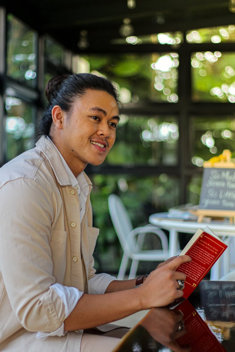 Smiling Man With Book At Table In Restaurant