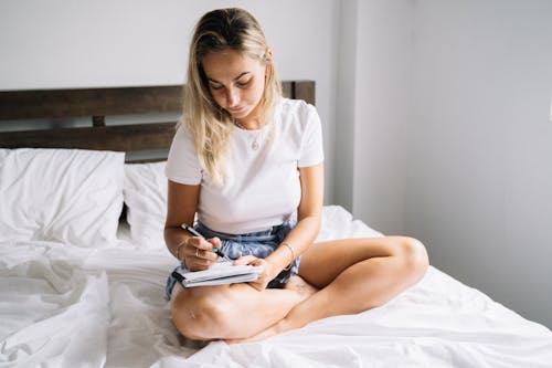 A Woman Writing in a Notebook while Sitting on Bed