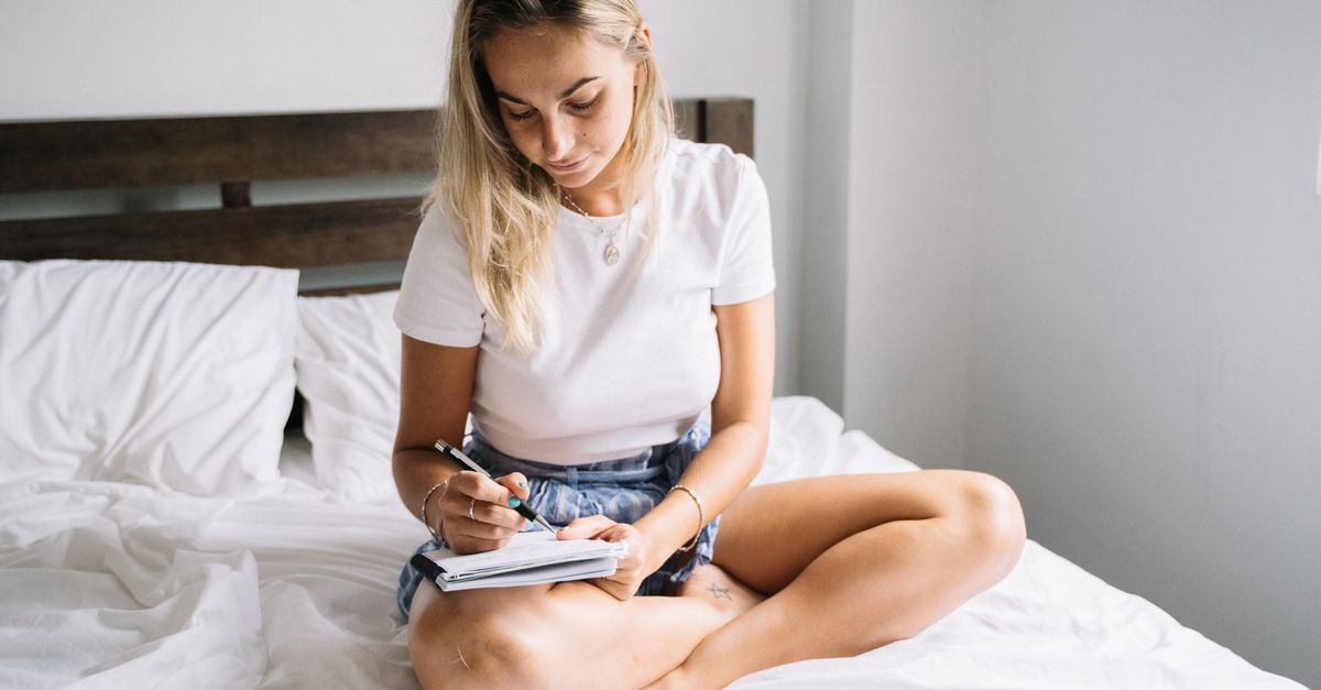 Woman sitting up in bed writing in a dream journal with morning light