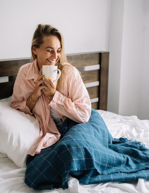 Woman Holding White Ceramic Mug Sitting on Bed