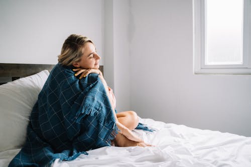 Woman Covered with a Blue Blanket Sitting on Bed 