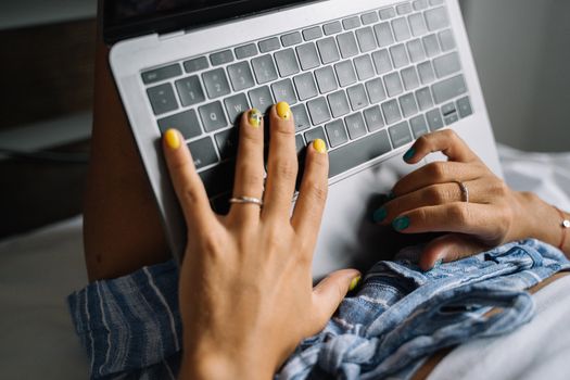 A close-up of hands with colorful nails typing on a laptop keyboard.