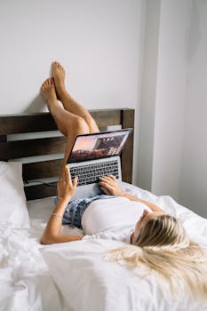 在舒适的卧室里，一位年轻女子躺在床上，用笔记本电脑放松身心