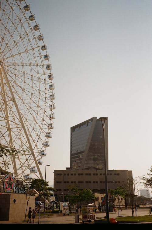 From below of observation wheel near contemporary building exterior in city under sky