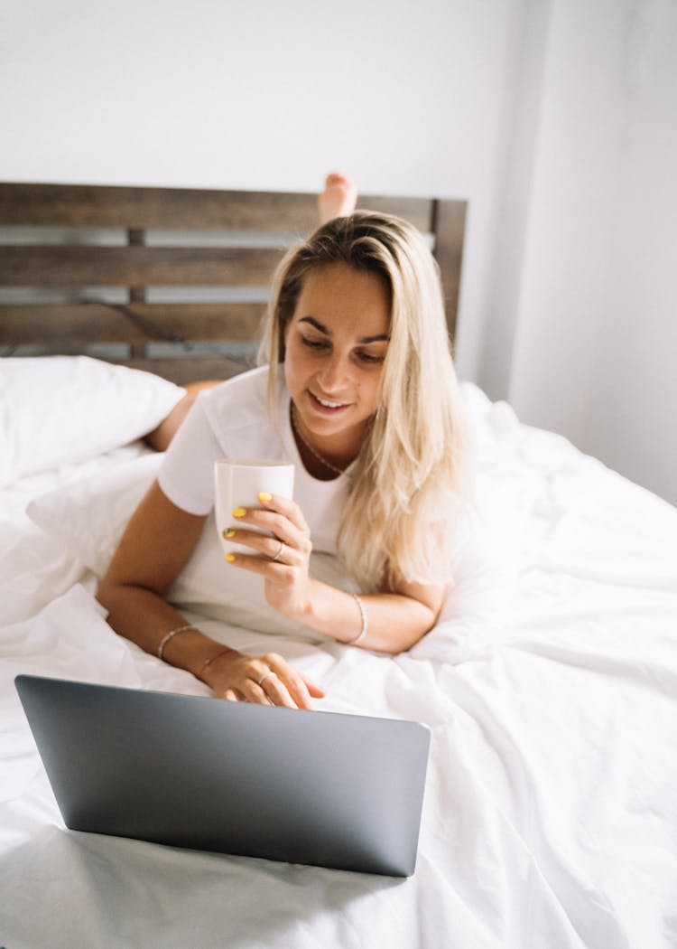 A Woman Lying On The Bed While Using A Laptop