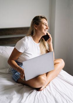 开朗的女人在家里用笔记本电脑在床上工作，电话放在一旁