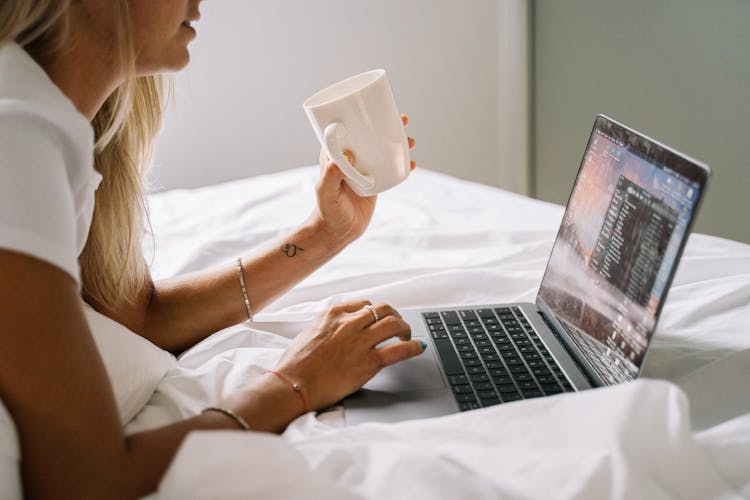 Woman With White Mug Using Laptop On Bed