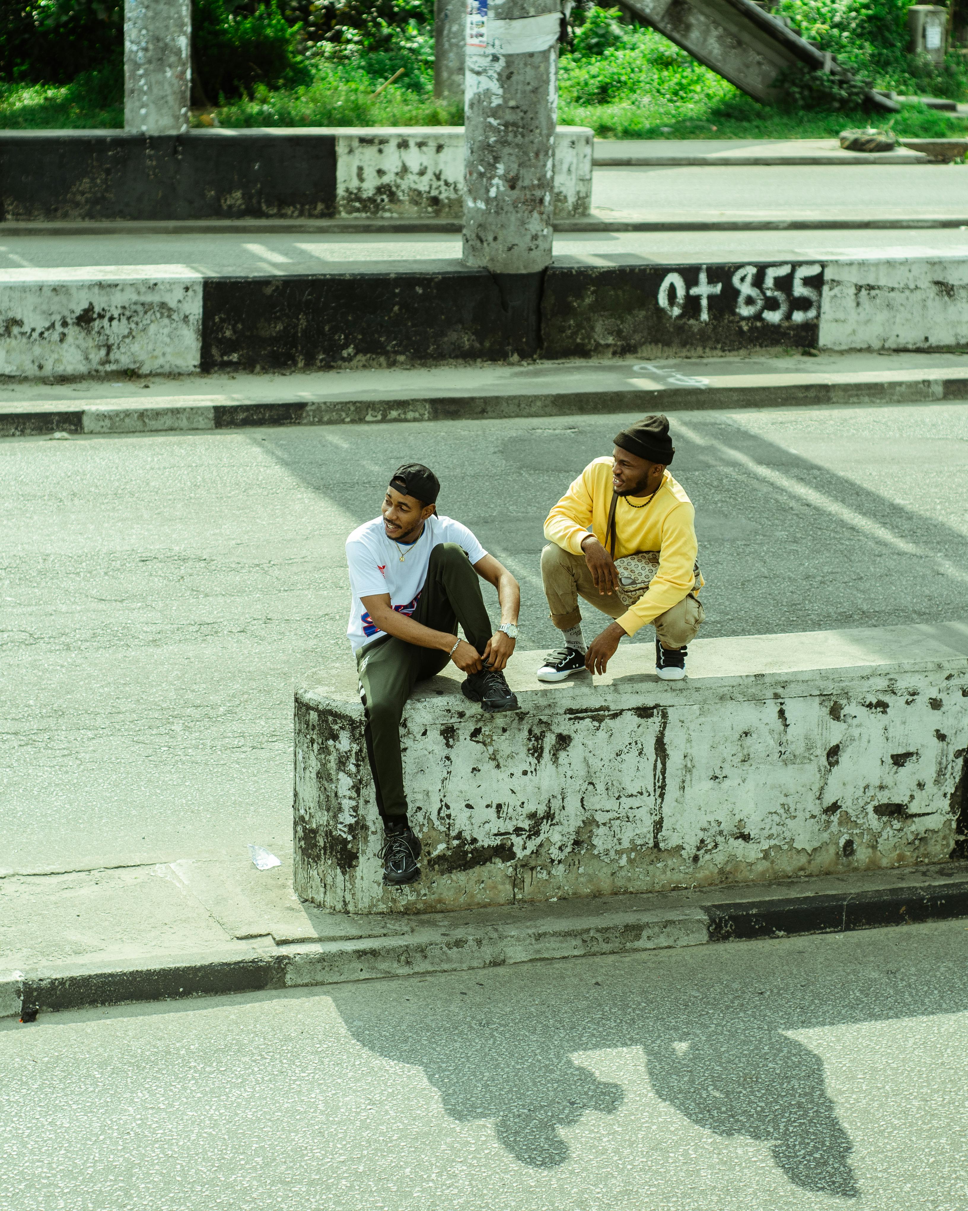From above full length content African American males in street style resting on concrete highway barrier and chatting on sunny summer weather