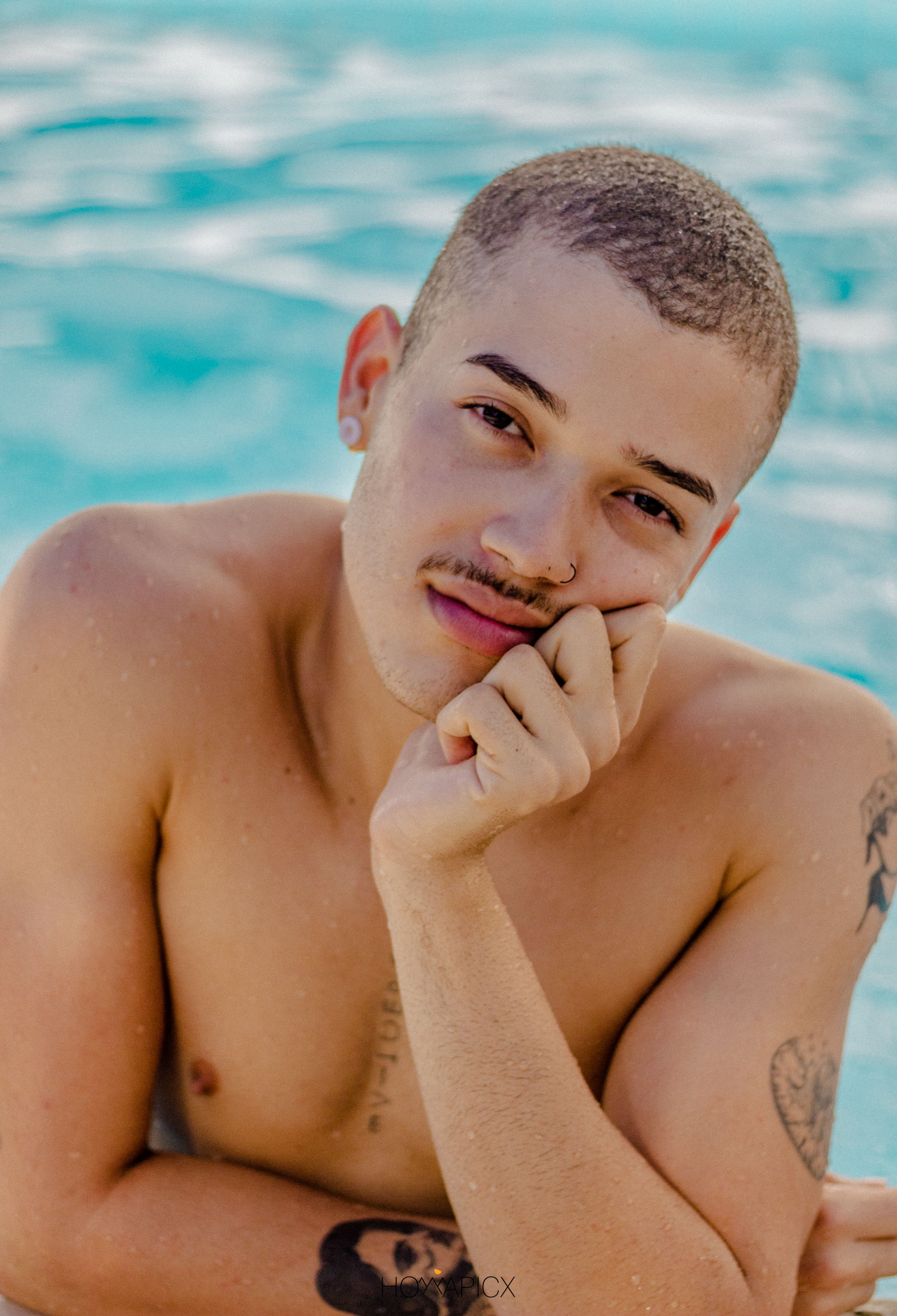 Close-up portrait of a young tattooed man posing by the pool.