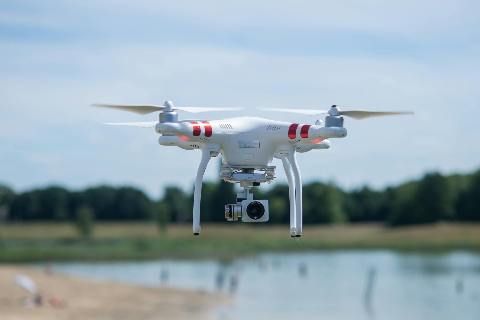 Aerial shot of a white drone with a camera hovering over a scenic landscape on a sunny day.