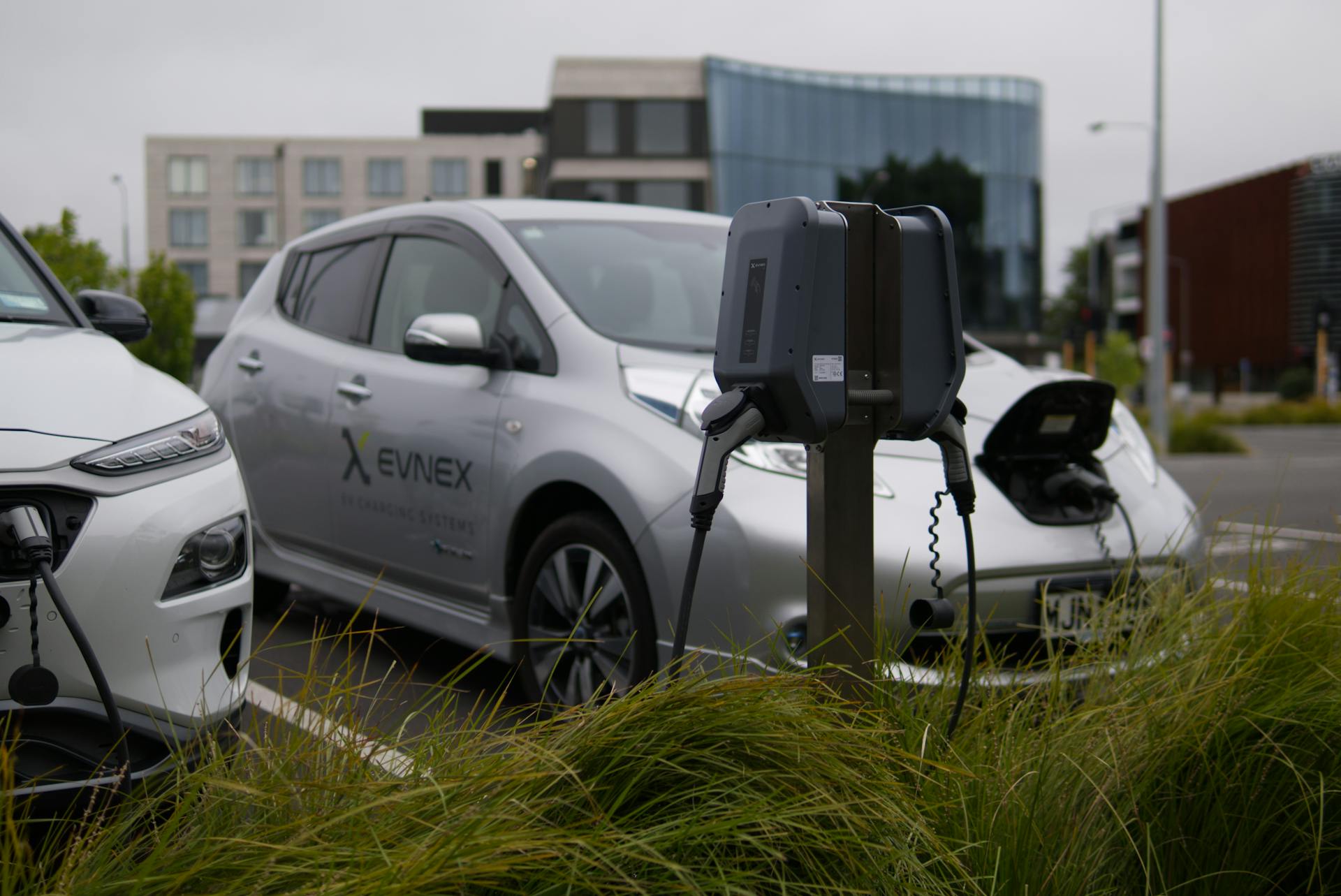 Electric vehicles at a charging station in Christchurch parking lot with modern architecture.