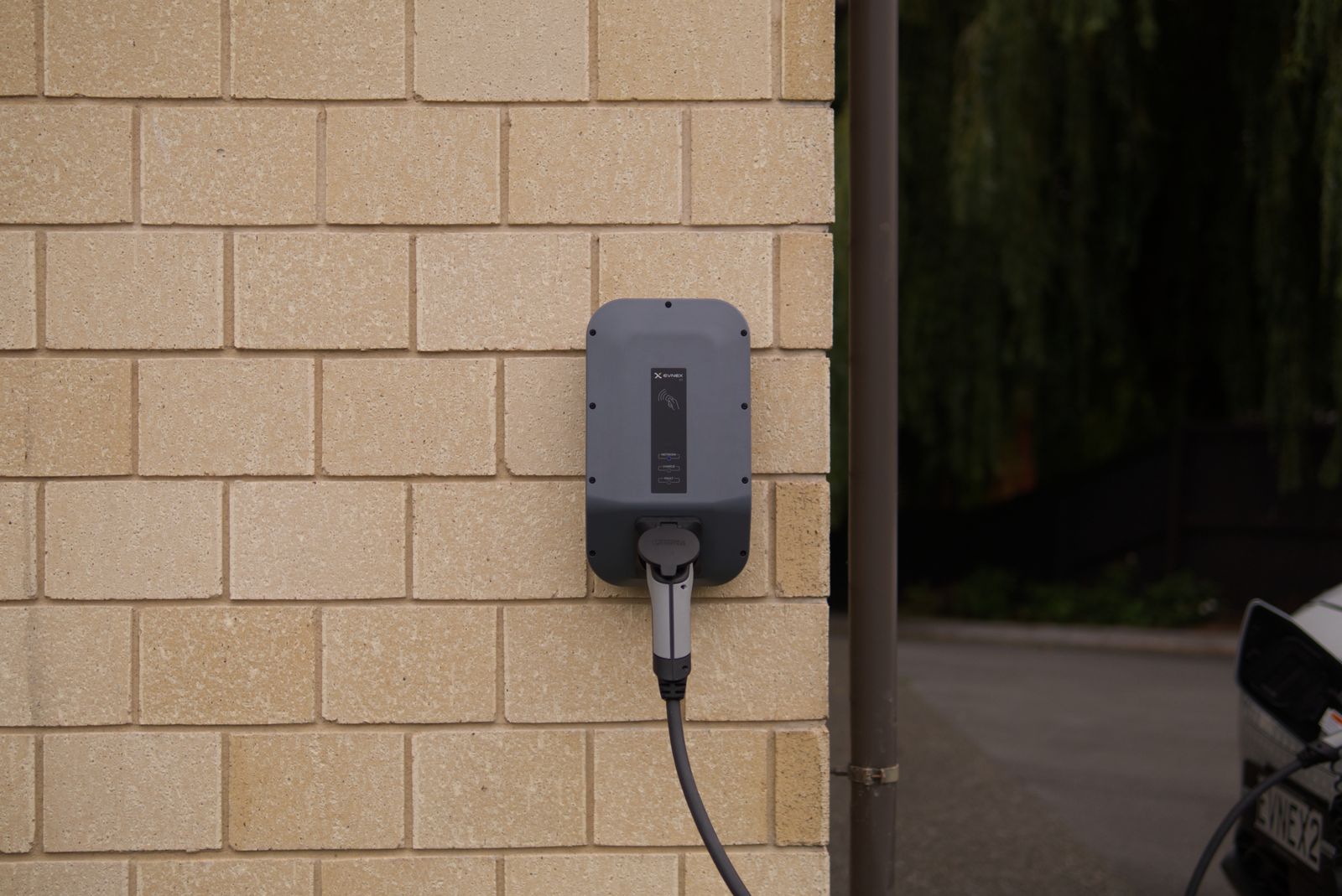 Home charging unit with the cable running to a car on the drive