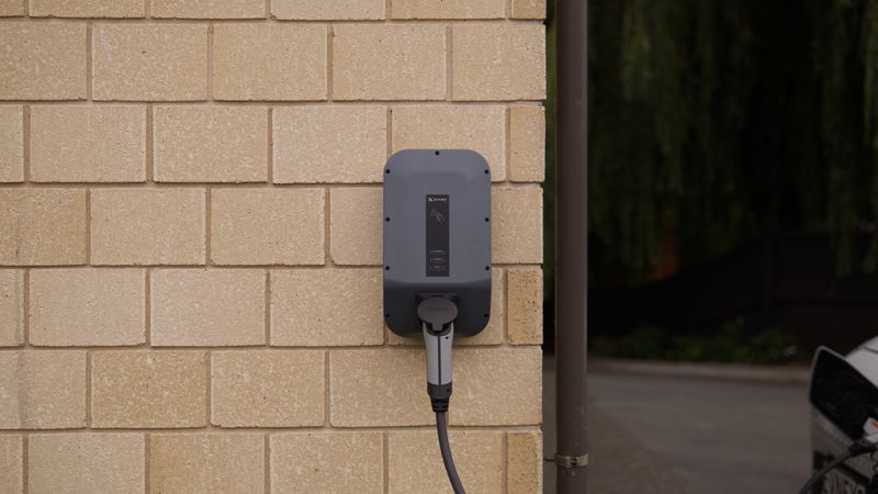 Level 2 EV charger mounted on the outside wall of a brick house with the cable plugged into a white electric vehicle
