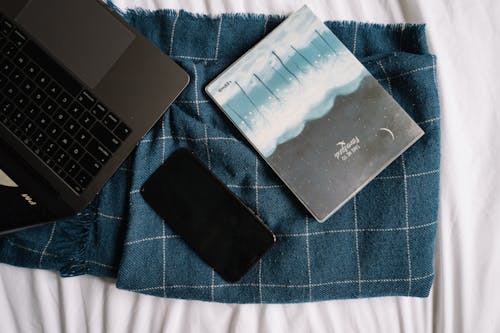 Laptop, Cellphone and a Notebook on Blue Blanket