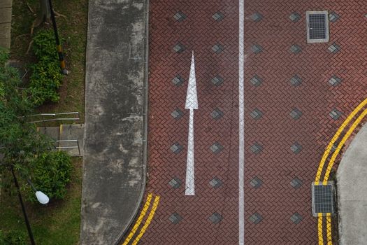 High-angle view of a white directional arrow on a textured brick pathway in Singapore.