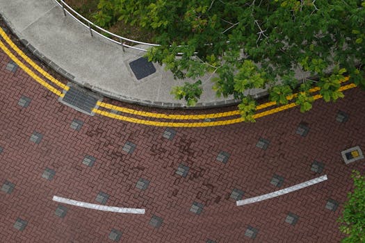 High-angle shot of a curved city street with greenery, brick pattern, and road markings.