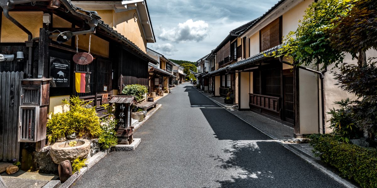 Explore a serene traditional Japanese street lined with historic wooden houses under a clear blue sky.