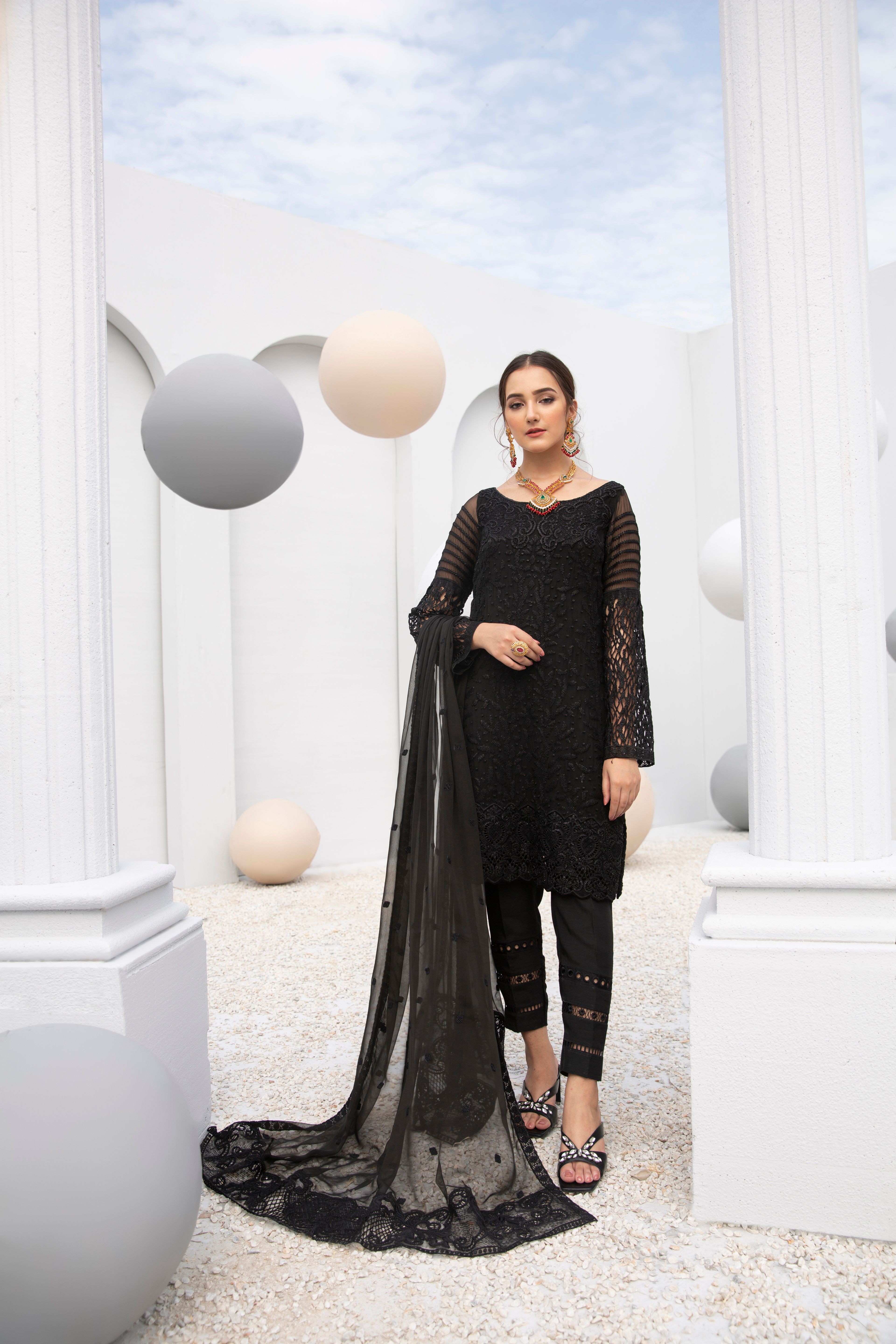 Portrait of an elegant woman in a black dress posing amidst white pillars and balloons.