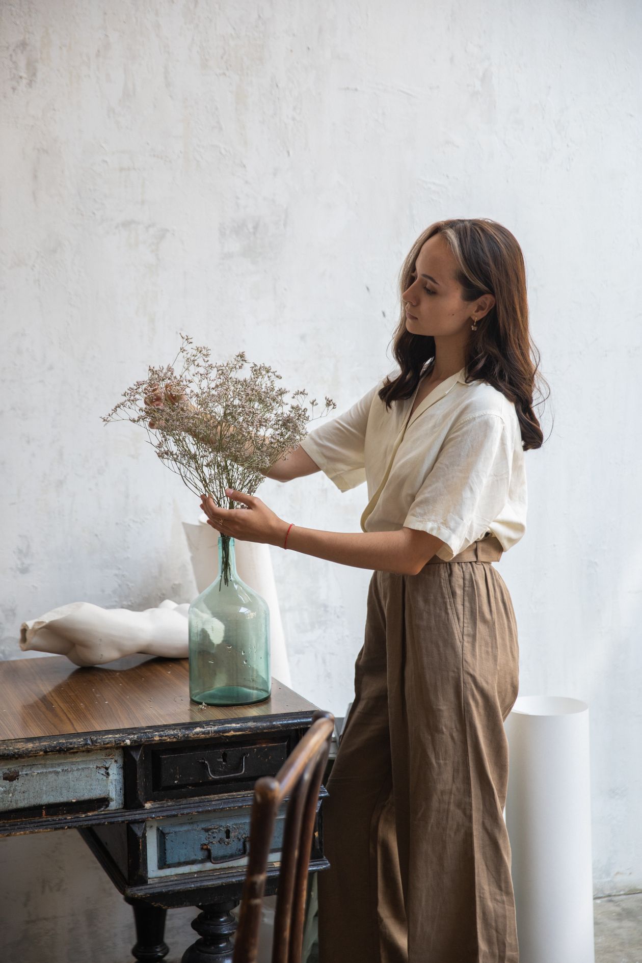 Woman in a cream linen shirt and brown wide-leg linen pants arranging flowers