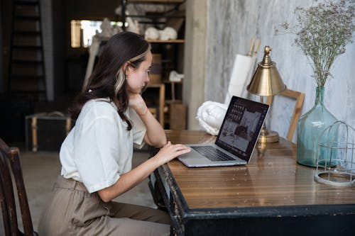 Free Woman in White Top Using Her Macbook on Wooden Table Stock Photo