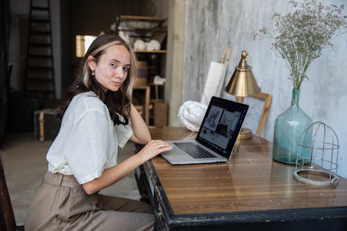 Woman in White Top Using Her Macbook on Wooden Table